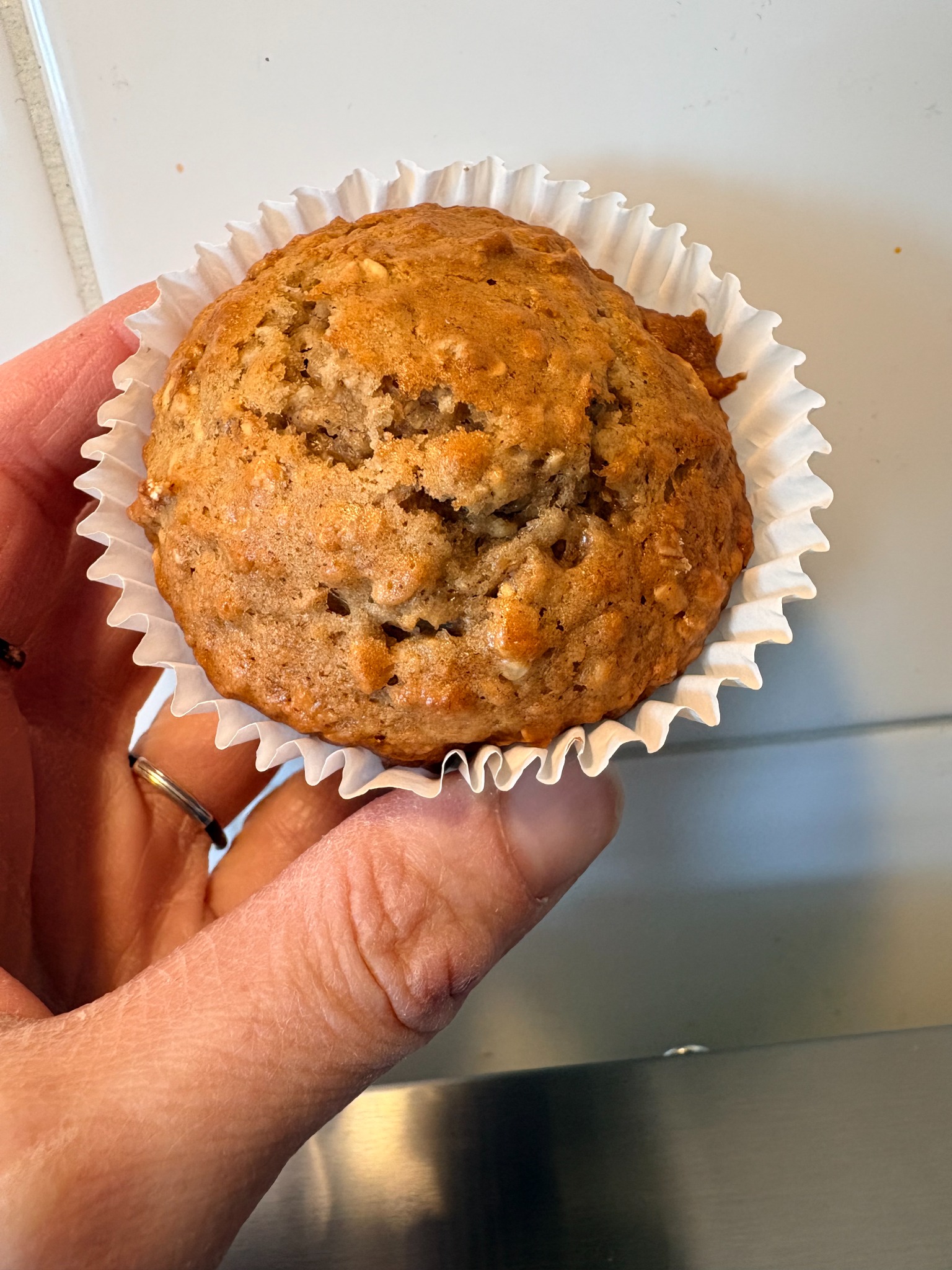 A golden maple brown sugar oatmeal muffin in a white paper liner, held in one hand.